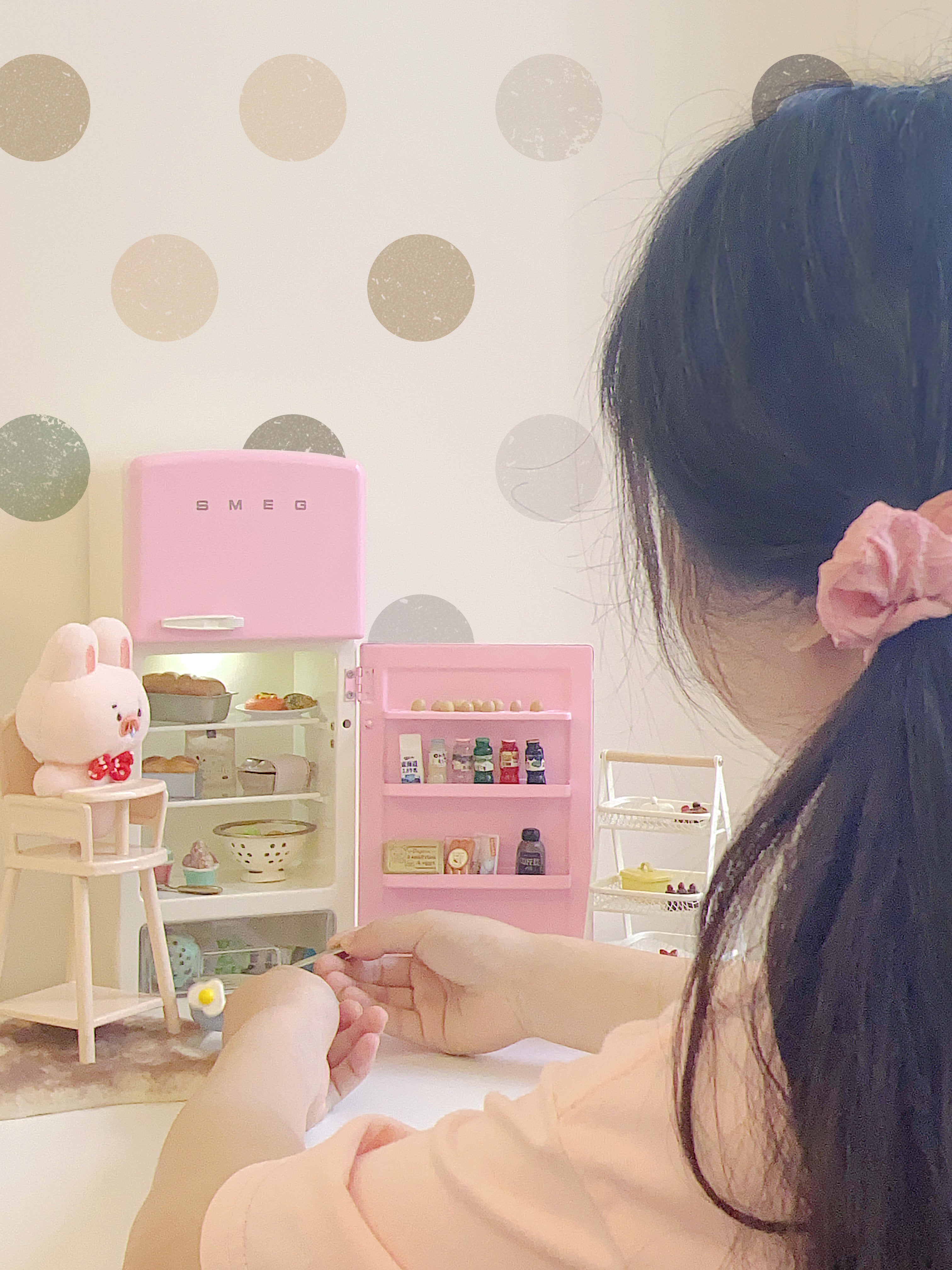 Open pink dollhouse refrigerator in a play scene with doll, chair and miniature food props not included